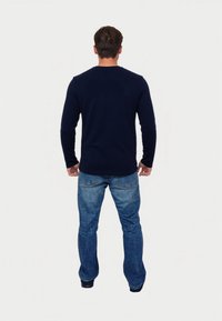 Námornícky modrá košeľa s dlhým rukávom a okrúhlym výstrihom, v kombinácii so svetlomodrými džínami. Štýl košele vyzerá hladko a džínsy majú klasický strih.