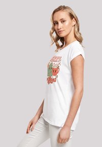 Weißes T-Shirt mit kurzen Ärmeln, das eine verspielte Grafik eines grünen Weihnachtsbaums und einer roten Tasse mit Kakao zeigt, akzentuiert mit buntem Text und Blumen.