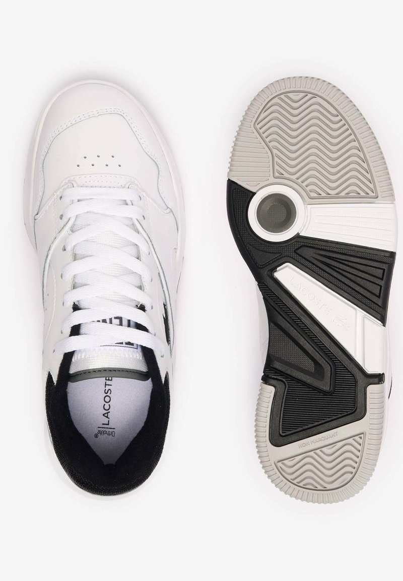 Baskets de sport en cuir blanc avec un accent en suède noir, lacets plats, perforations et une semelle en caoutchouc texturé noir et gris.