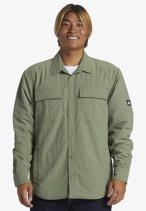 Green button-up shirt made of lightweight fabric, featuring two large chest pockets, snap closures, and long sleeves.