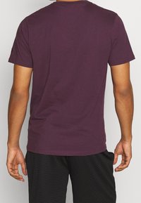 Lila kortärmad t-shirt med rund halsringning, gjord av mjuk tyg, med en slät yta. Bärs med svarta texturerade shorts.