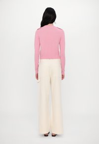 Pull en maille rose clair ajusté avec un ourlet à côtes et des détails aux épaules, associé à un pantalon crème ample avec des poches latérales.