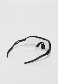 Schwarze Sportsonnenbrille mit einem leichten Rahmen, klaren Gläsern und flexiblen Bügeln, die mit gummierten Enden für Komfort und Halt ausgestattet sind.