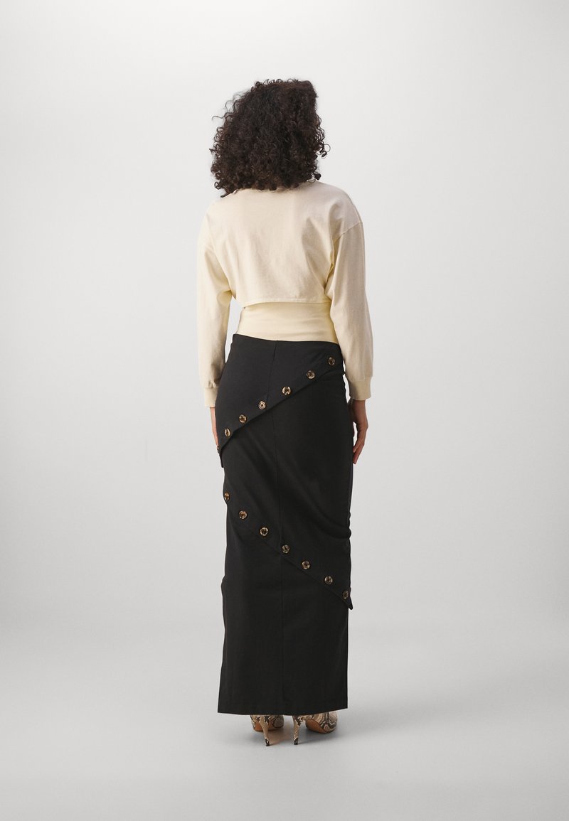 Jupe longue noire avec un design de drapé diagonal, accents en métal doré, et un sweat-shirt cropped de couleur claire.
