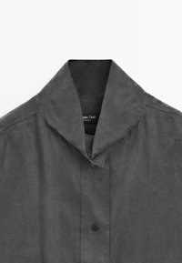 Gray jacket with a distinct collar design, featuring a button closure and smooth texture. Label visible inside collar area.