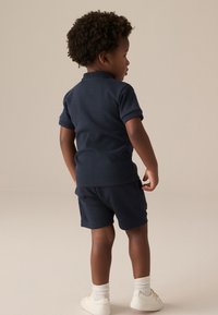 Polo en coton bleu marine à manches courtes, associé à un short assorti. Présente une texture subtile et un col rond classique.