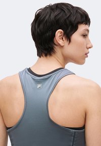 Personne aux cheveux courts et foncés portant un débardeur gris dos nageur montrant le haut du dos et le profil du visage.