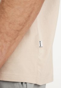 Beige bomulds t-shirt med korte ærmer, sideetiket og diskrete syninger. Glat tekstur med en afslappet pasform.