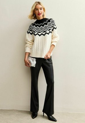 Maglione bianco lavorato a maglia con un motivo geometrico nero, abbinato a pantaloni in similpelle neri e una clutch argento. Tacchi neri a punta.