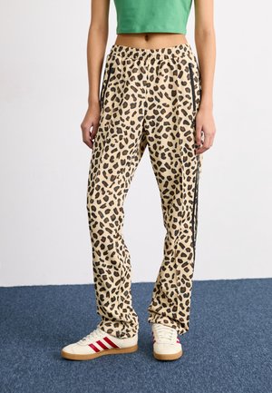 Leopard print loose-fit pants with black side stripes worn with white sneakers featuring red stripes and gum soles.