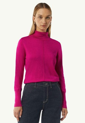 Fuchsia-Rollkragenpullover mit langen Ärmeln, versehen mit einer Nahtdetail vorne und einer taillierten Passform, kombiniert mit dunklen Jeans.