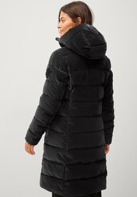 Zwarte pufferjas met capuchon, voorzien van een geborduurde patroon op de stof. Inclusief een geborduurde detail op de mouw.