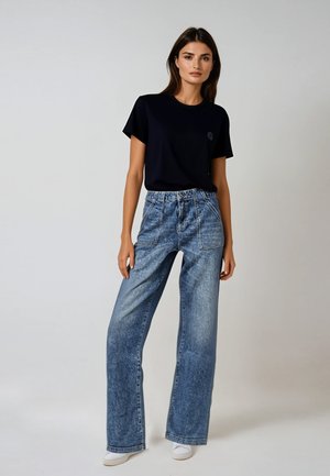 Navy T-shirt with short sleeves and a small logo, paired with high-waisted, wide-leg, light blue jeans and white sneakers.