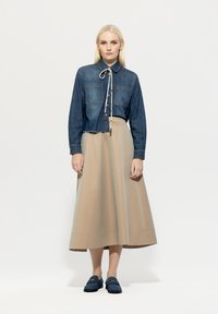 Denim button-up shirt with long sleeves and chest pockets, paired with a beige ankle-length skirt and blue slip-on shoes. Minimalist design.