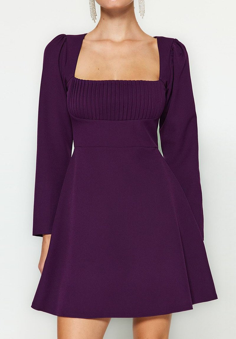 Robe violette avec un décolleté carré, un corsage côtelé, de longues manches bouffantes et une jupe évasée. Tissu lisse avec une silhouette fluide.