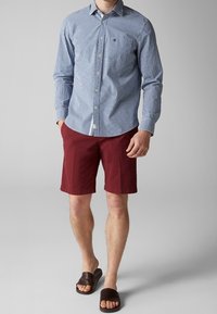 Niebiesko-biała koszula w kratę zapinana na guziki, czerwone szorty, brązowe sandały typu klapki. Cechuje się kontrastowymi kolorami i wzorami oraz swobodnym krojem.