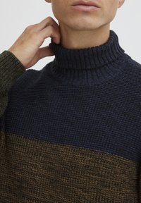 Maglione con collo e alto in maglia grossa, caratterizzato da una parte superiore blu scuro e una parte inferiore marrone con motivi testurizzati. Dettaglio del colletto a coste.