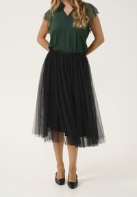 Black tulle skirt with a soft, flowing design, paired with a green top featuring lace sleeves and a V-neckline. Black shoes complete the look.