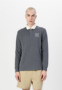 Polo majica s dugim rukavima v temno sivi bombaž s ovratnikom v kremni barvi in vezenim logotipom "H" na levem prsnem delu. Preprost dizajn, sproščen kroj.