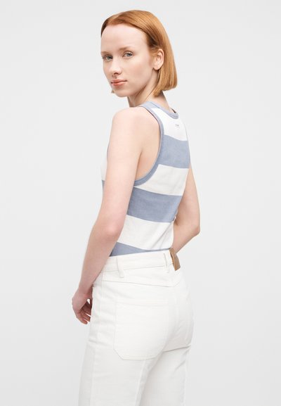 Débardeur blanc à rayures horizontales bleues, avec un col rond et de larges emmanchures. Modèle portant un pantalon blanc taille haute.