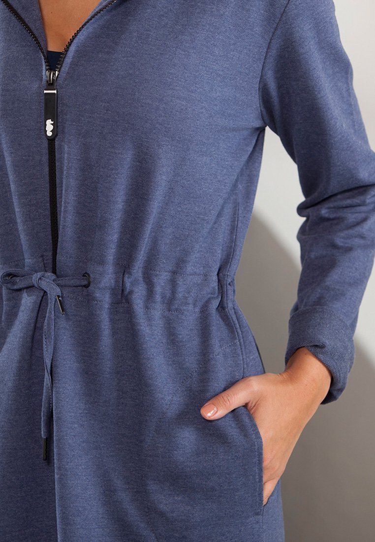 Granatowy kombinezon na zamek błyskawiczny z miękkiego, elastycznego materiału. Posiada regulowany pas, długie rękawy i boczne kieszenie. Wykończony czarnym zamkiem.