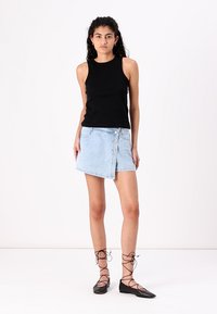 Black ribbed tank top, light blue denim wrap skirt with button details and distressed accents, paired with black lace-up flats.