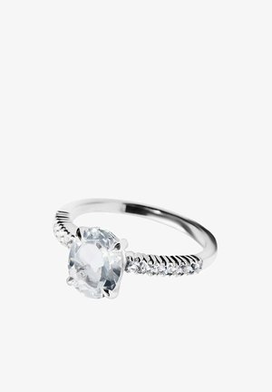 Anillo de plata con una gran piedra preciosa redonda y transparente en el centro y piedras pequeñas transparentes incrustadas a lo largo de la banda sobre un fondo blanco.