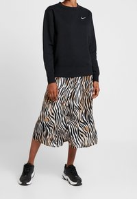 Sweatshirt noir à col rond et logo, associé à une jupe fluide rayée zèbre en noir, blanc et beige. Porté avec des baskets noires.