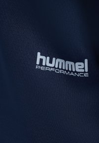Zbliżenie na granatową tkaninę z białym nadrukiem logo "hummel PERFORMANCE".
