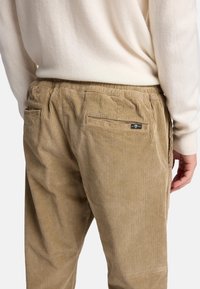 Cordura-Hosen in einem hellbraunen Farbton, mit einem strukturierten Rippmuster, elastischem Bund und zwei Gesäßtaschen mit einem Markenetikett.
