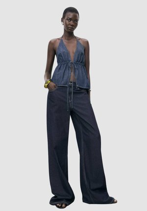 Denim halter top with tie front and puffed bodice; paired with wide-leg dark denim pants featuring contrast stitching and a relaxed fit.