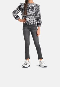 Felpa a righe in bianco e nero con spalle a palloncino, abbinata a jeans skinny grigi con orli sfilacciati e sneaker bianche con dettagli neri.