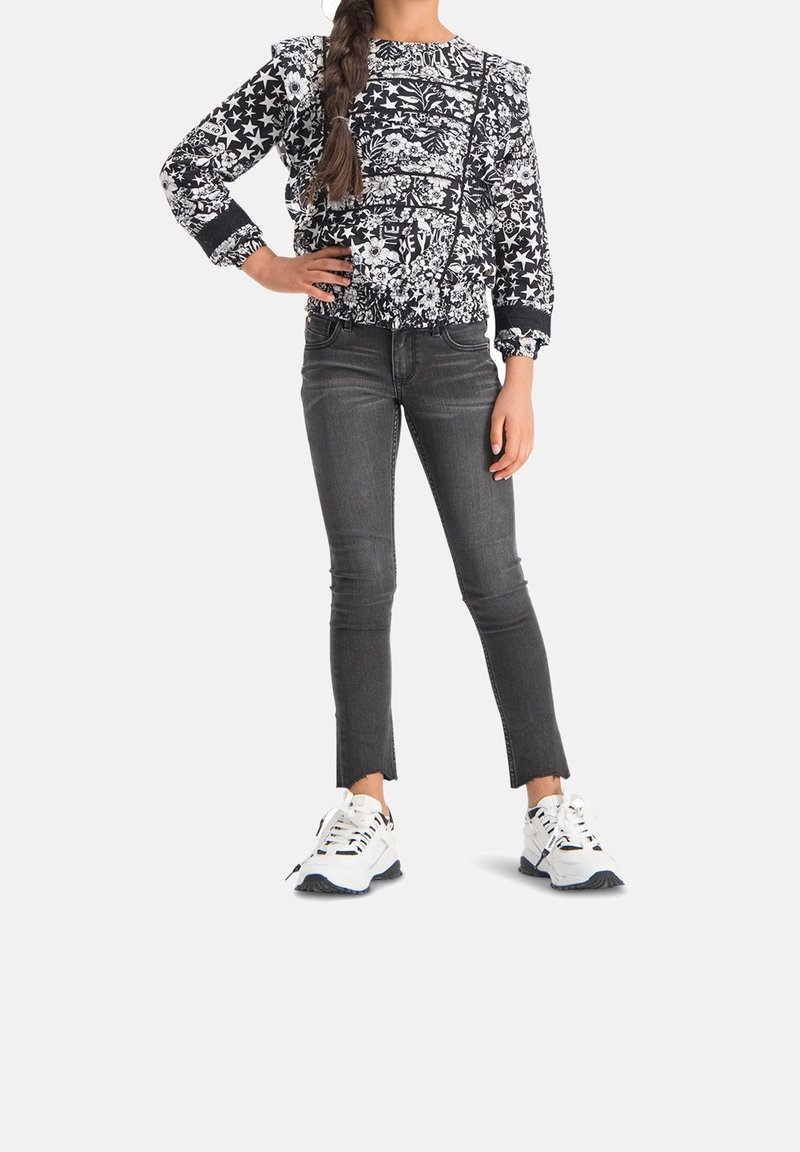 Felpa a righe in bianco e nero con spalle a palloncino, abbinata a jeans skinny grigi con orli sfilacciati e sneaker bianche con dettagli neri.