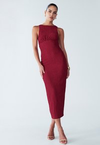 Midi obleka z teksturo in rebrastim vzorcem v globoki bordo barvi, z visokim ovratnikom in prilegajočim pasom, s pravokotno silhueto in rahlim nabiranjem.