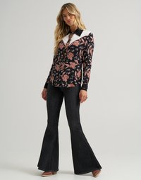 Langermet blomstret skjorte med hvit krage og svarte detaljer, kombinert med flared mørk denim jeans. Glatt stoff med livlige mønstre.