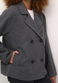Grau gemischter Woll-Doppelreiher mit Reverskragen, schwarzen Knöpfen und seitlichen Taschen, mit relaxtem Schnitt und weicher Textur.