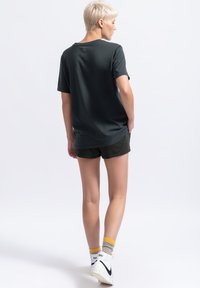 Diepgroene katoenen t-shirt met korte mouwen, een ontspannen pasvorm en een klein detail op de achterkant. Draagt met donkere shorts en witte sneakers.