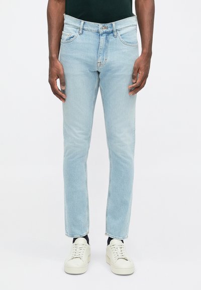 Svetlo modré denimové nohavice s úzkym strihom, obsahujúce päť vreciek, zapínanie na gombík a mierne vyblednutie. Skombinované s off-white teniskami.