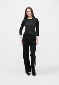 Musta pitkähihainen paita yhdistettynä väljien mustien housujen kanssa, joissa hopeiset sivukoristeet. Valmistettu pehmeästä kankaasta ja rento istuvuus.