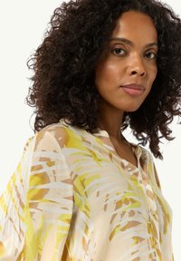 Lightweight, semi-transparent blouse in cream with yellow and brown palm leaf print, featuring a button-down front and V-neckline.