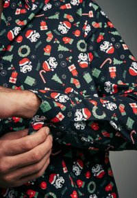 Dlouhý rukáv tričko vyrobené z tmavé tkaniny s vánočním vzorem bílých ledních medvědů, vánočních stromků, dárků a cukrových hůlek.