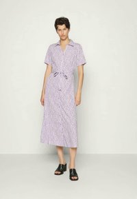 Vestido curto de cor roxa clara, com mangas curtas e padrões florais, colarinho e cintura com laço. Comprimento até à metade da panturrilha, feito de tecido suave; combinado com sandálias pretas.