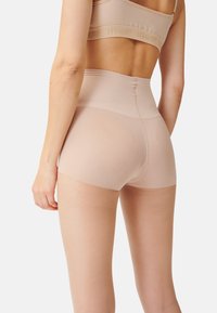 Beige, hochgeschnittene Shorts aus transparentem, dehnbarem Material, mit glatter Textur und minimalen Nähten für einen nahtlosen Look.