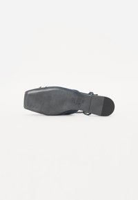 Chaussure plate noire texturée avec un bout arrondi, dotée d'une semelle en caoutchouc lisse et de détails de laçage sur la partie supérieure.