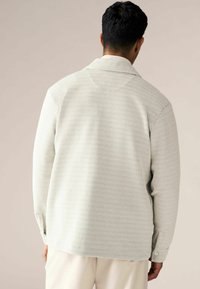 Jachetă tricotată de culoare gri deschis, cu un model texturat, cu țesătură deschisă, mâneci lungi și un design cu guler, văzută din spate.
