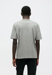 Γκρι βαμβακερό t-shirt με άνετη εφαρμογή, κοντά μανίκια και στρογγυλή λαιμόκοψη. Λείος υφασμάτινος χαρακτήρας, μινιμαλιστικός σχεδιασμός, προβάλλεται η πίσω όψη.