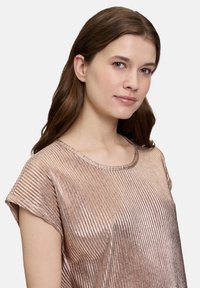 Metallisch roségoldenes Oberteil mit gerippter Textur, kurzen Ärmeln und Rundhalsausschnitt, das das Licht reflektiert und zusätzlichen Glanz verleiht.