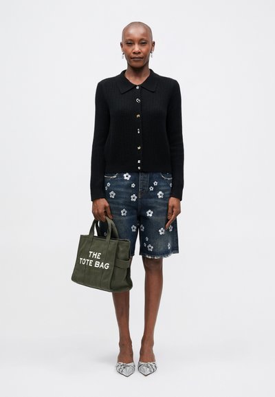 Cardigan negru cu nervuri și închidere cu nasturi, pantaloni scurți din denim albastru cu broderie florală albă, geantă verde cu textul "THE TOTE BAG", pantofi argintii.