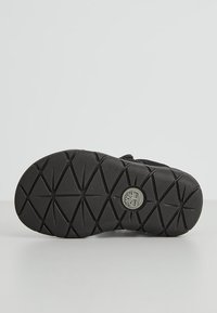 Sole di scarpa nera con un motivo a diamante testurizzato, caratterizzata da un logo circolare al centro. Il materiale sembra essere in gomma per garantire durata.
