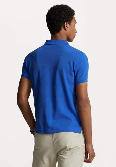 Camisa polo azul con un diseño de tejido texturizado, mangas cortas y un cuello clásico, combinada con pantalones claros de corte relajado.